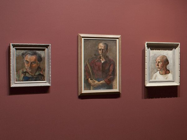 Three framed portraits on a muted red wall