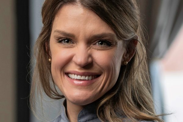 Headshot of a white woman with light brown hair, smiling for the camera and wearing a grey chef's jacket