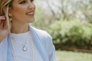 profile of a woman with blonde hair wearing a blue jacket and white shirt with two strands of pearls and a gold and pearl necklace