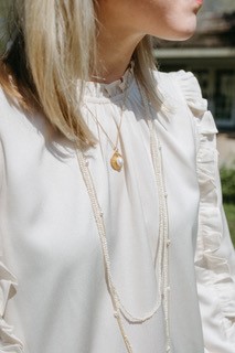 Torso of a woman with a white blouse wearing a long strand of pearls and a gold and pearl necklace