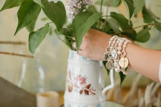 White vase with greenery, held by a woman's wrist with several pearl bracelets