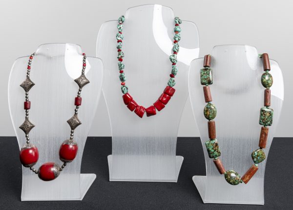 Three necklaces displayed on clear acrylic holders with beads in red and green