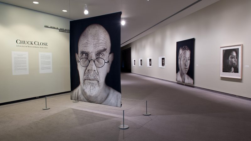 Gallery installation image of overside portraits accompanied by smaller photographs of the subjects