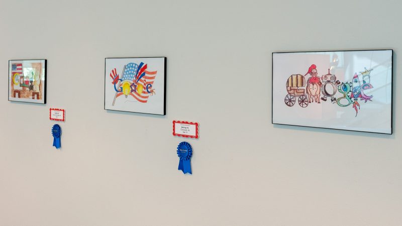 Gallery image showing three entries in Doodle for Google. Blue ribbons are displayed to the lower right of the framed artworks