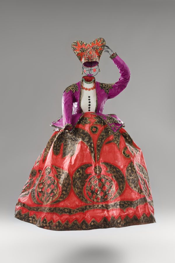 Wire mannequin wearing a red headpiece and a fitted purple jacket over a white shirt over a full red skirt with brown accents.