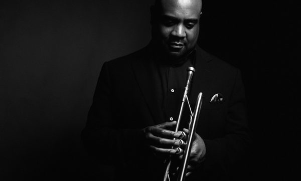 Photo of a Black man wearing a black suit and holding a trumpet