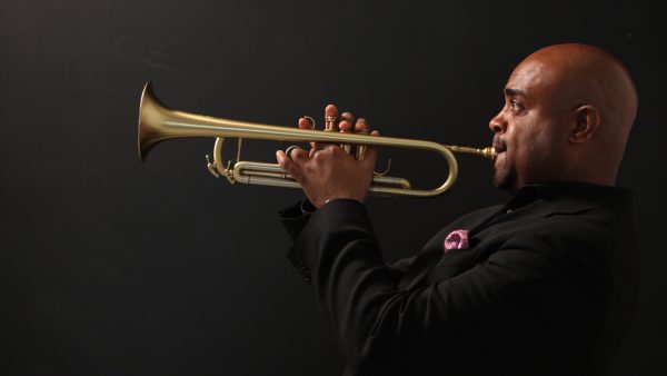 Photo of a Black man wearing a black suit and holding a trumpet