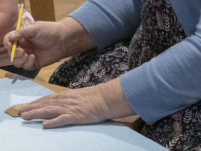 Woman's hands holding a pencil over a light blue paper on a table