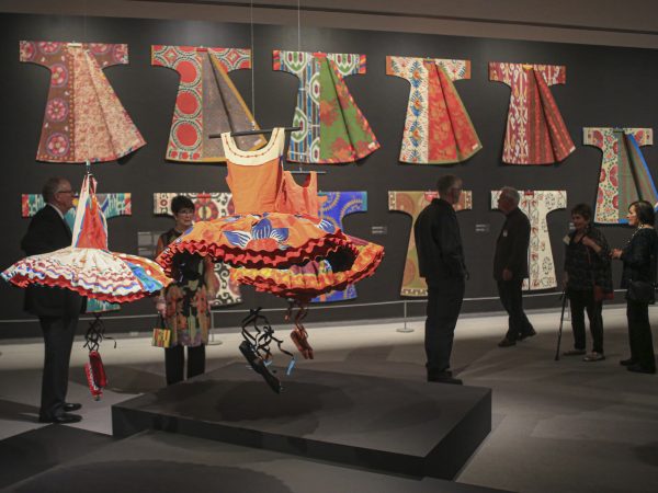 Six museum visitors in the galleries standing near the tutus and kaftans from the exhibition 