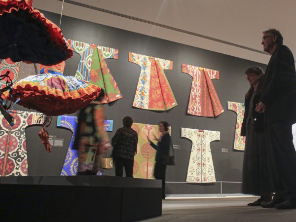Two visitors stand off to the right while viewing the paper tutus in the exhibition 