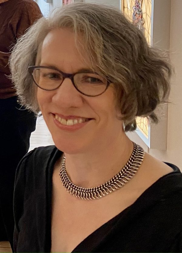 Woman with chin-lengthy light grey hair wearing glasses, a necklace and a black top