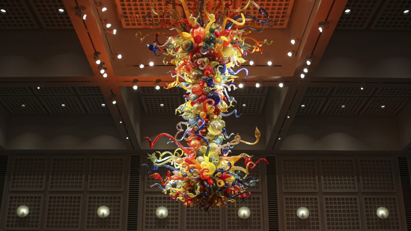 Photo of the Chihuly Chandelier at night with people sitting at tables and chairs underneath it