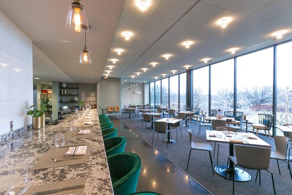 Interior photo of 1400 by Elderslie taken from the entrance to the restaurant and showing the bar space as well as tables and chairs near the floor-to-ceiling windows overlooking the Art Garden