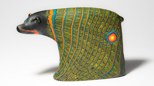 Glass art of a black bear with the body covered in a geometic lined pattern of green, turquoise and orange.