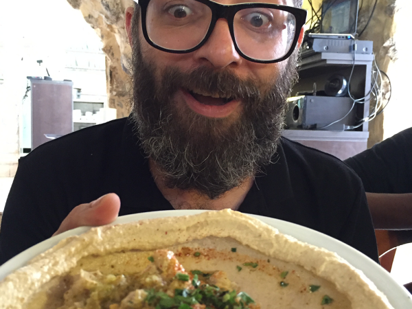Photo for Hummus the Movie. The Host is wide-eyed, excited about showing a large plate of hummus.