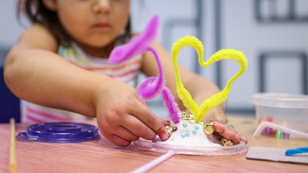 Shot of little girl with a craft made out of colorful pipe cleaners. The little girl is out of focus, while the art is in focus.