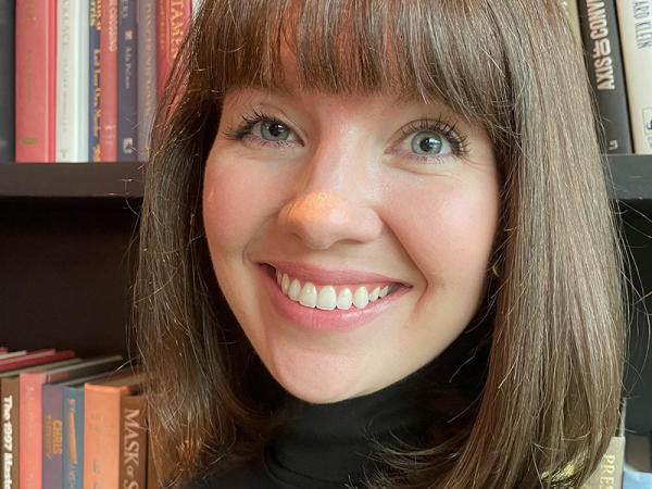Photo of a woman with short hair and bangs, standing in front of a bookshelf