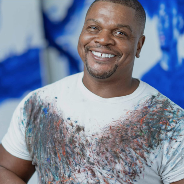 African American male artist Kehinde Wiley, standing in front of a blue and white background